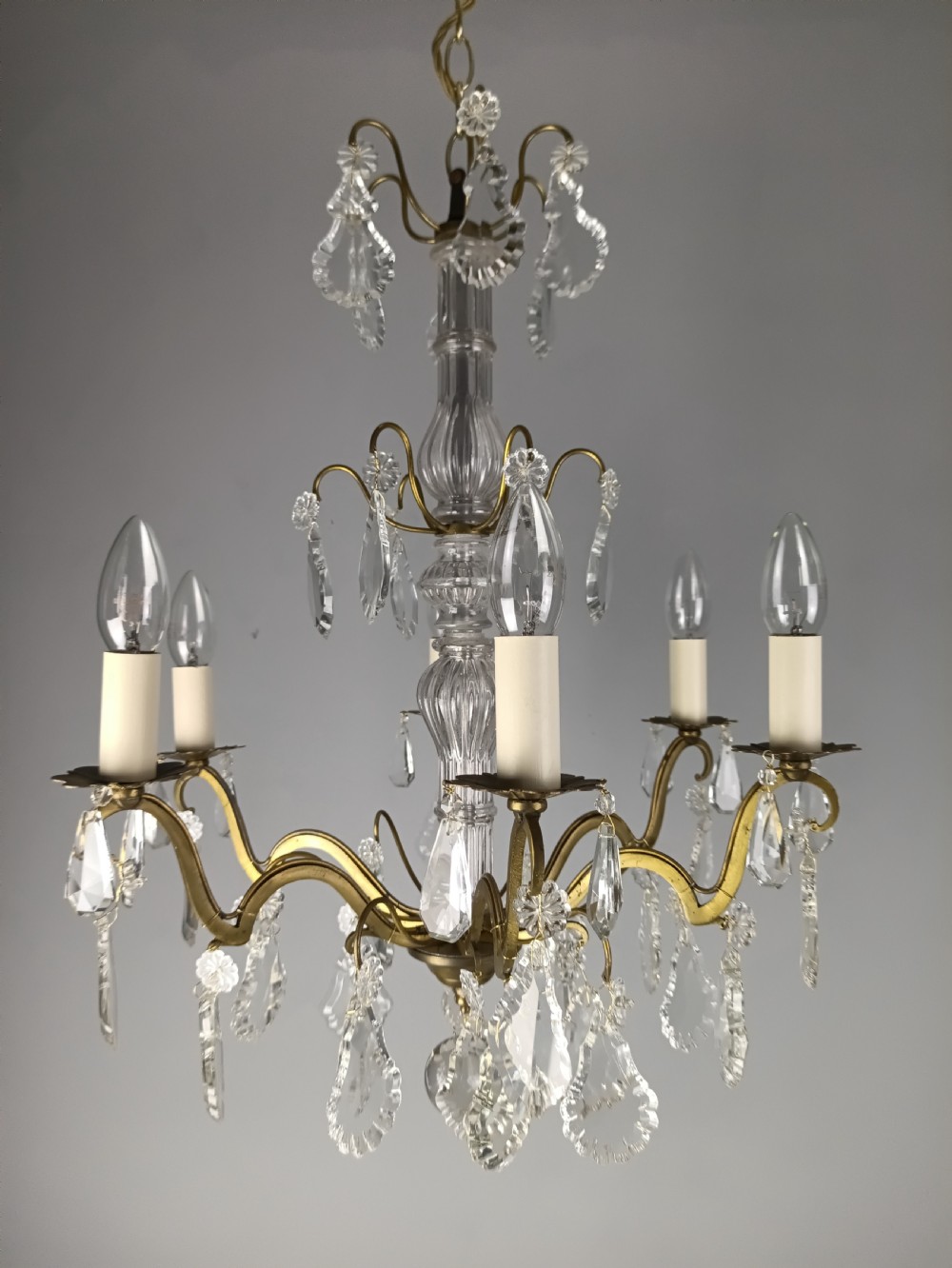 A French style gilt brass six arm chandelier embellished with clear glass stem sections and suspended crystal teardrop prisms. View XIV