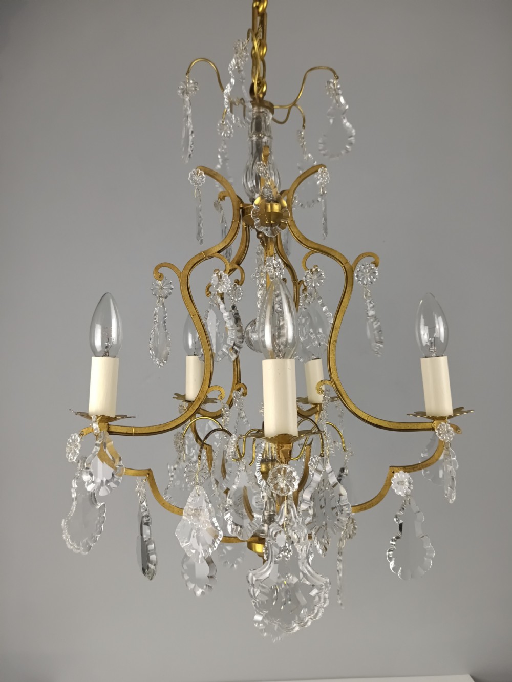 A French Rococo style birdcage chandelier crafted from gilded metal featuring five candle arms adorned with clear cut crystal drops and rosettes.