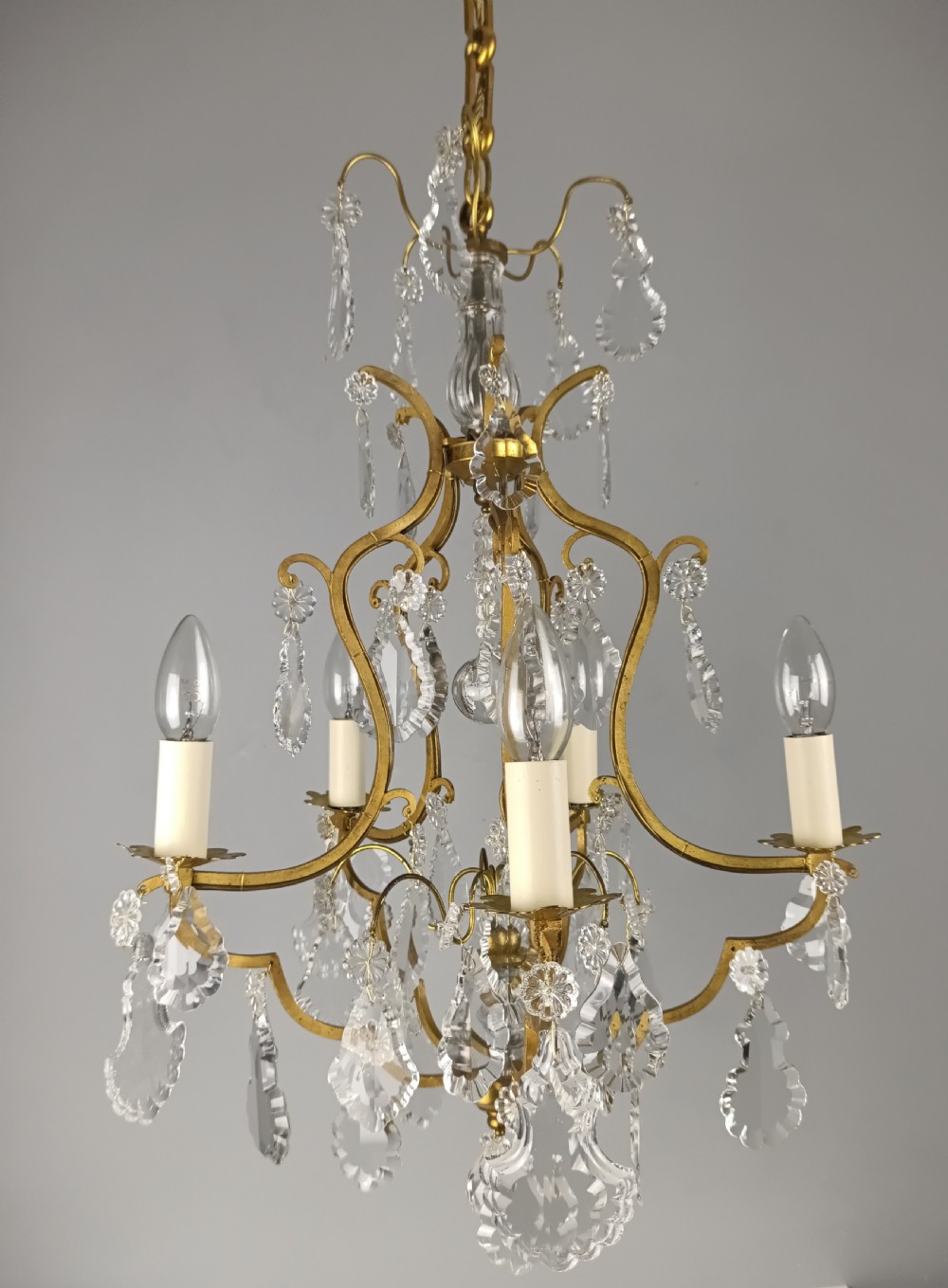 A French Rococo style birdcage chandelier crafted from gilded metal featuring five candle arms adorned with clear cut crystal drops and rosettes. View III