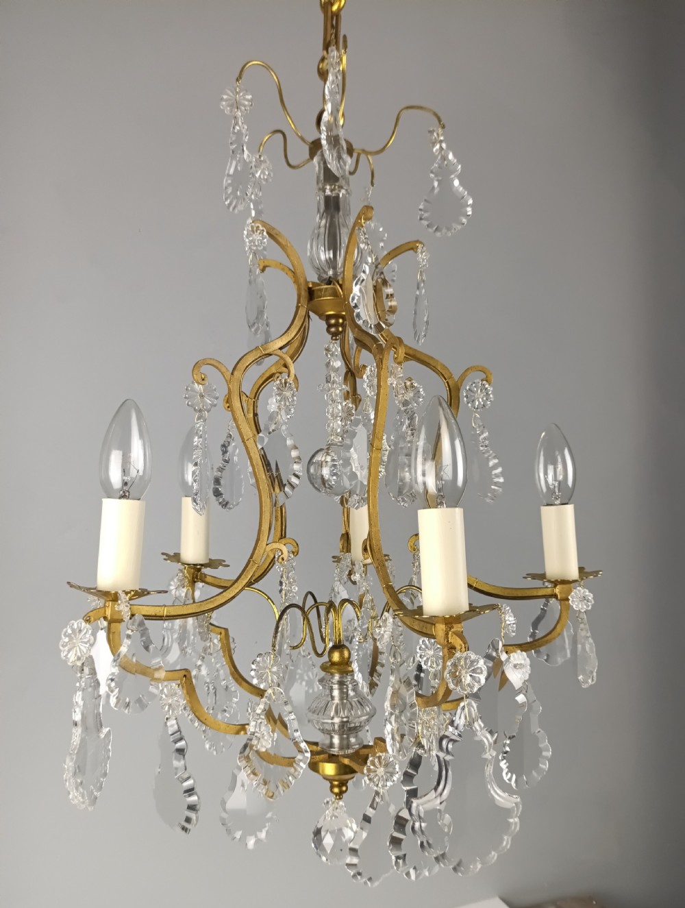 A French Rococo style birdcage chandelier crafted from gilded metal featuring five candle arms adorned with clear cut crystal drops and rosettes. View IV