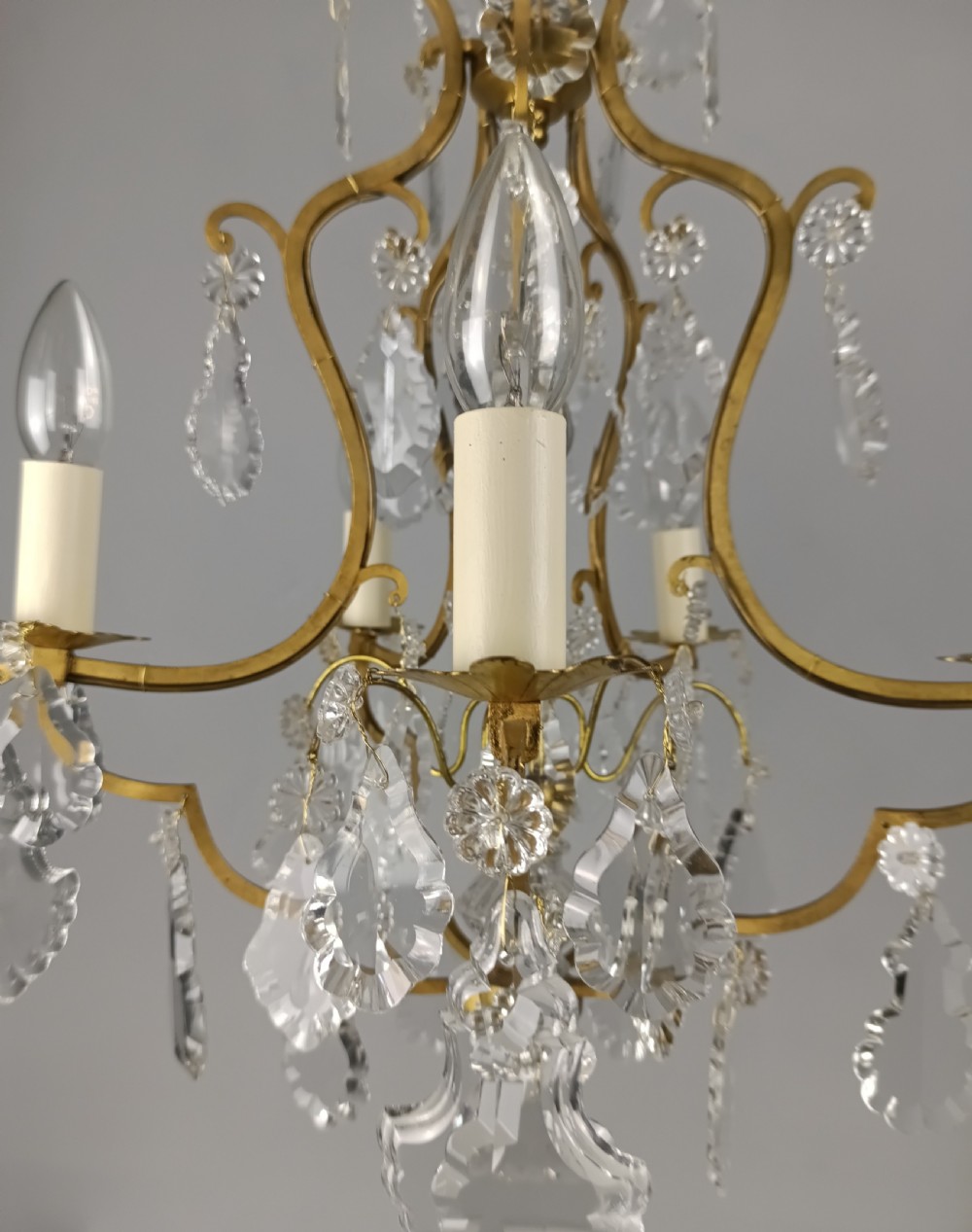 A French Rococo style birdcage chandelier crafted from gilded metal featuring five candle arms adorned with clear cut crystal drops and rosettes. View V