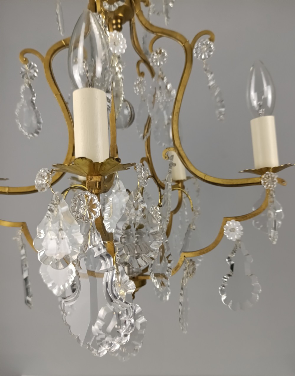 A French Rococo style birdcage chandelier crafted from gilded metal featuring five candle arms adorned with clear cut crystal drops and rosettes. View VI