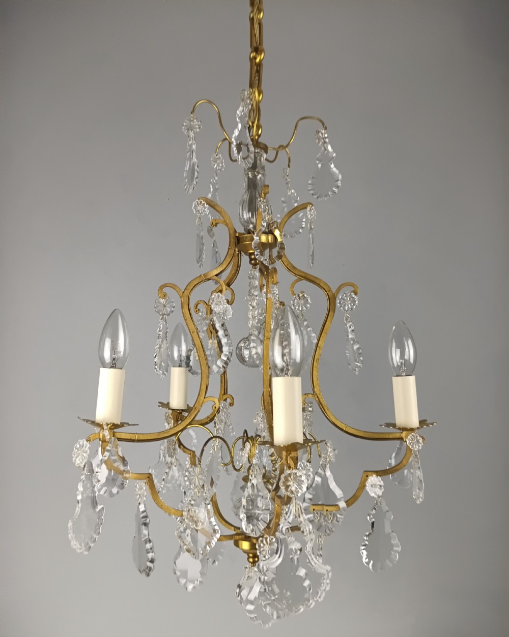 A French Rococo style birdcage chandelier crafted from gilded metal featuring five candle arms adorned with clear cut crystal drops and rosettes. View VII
