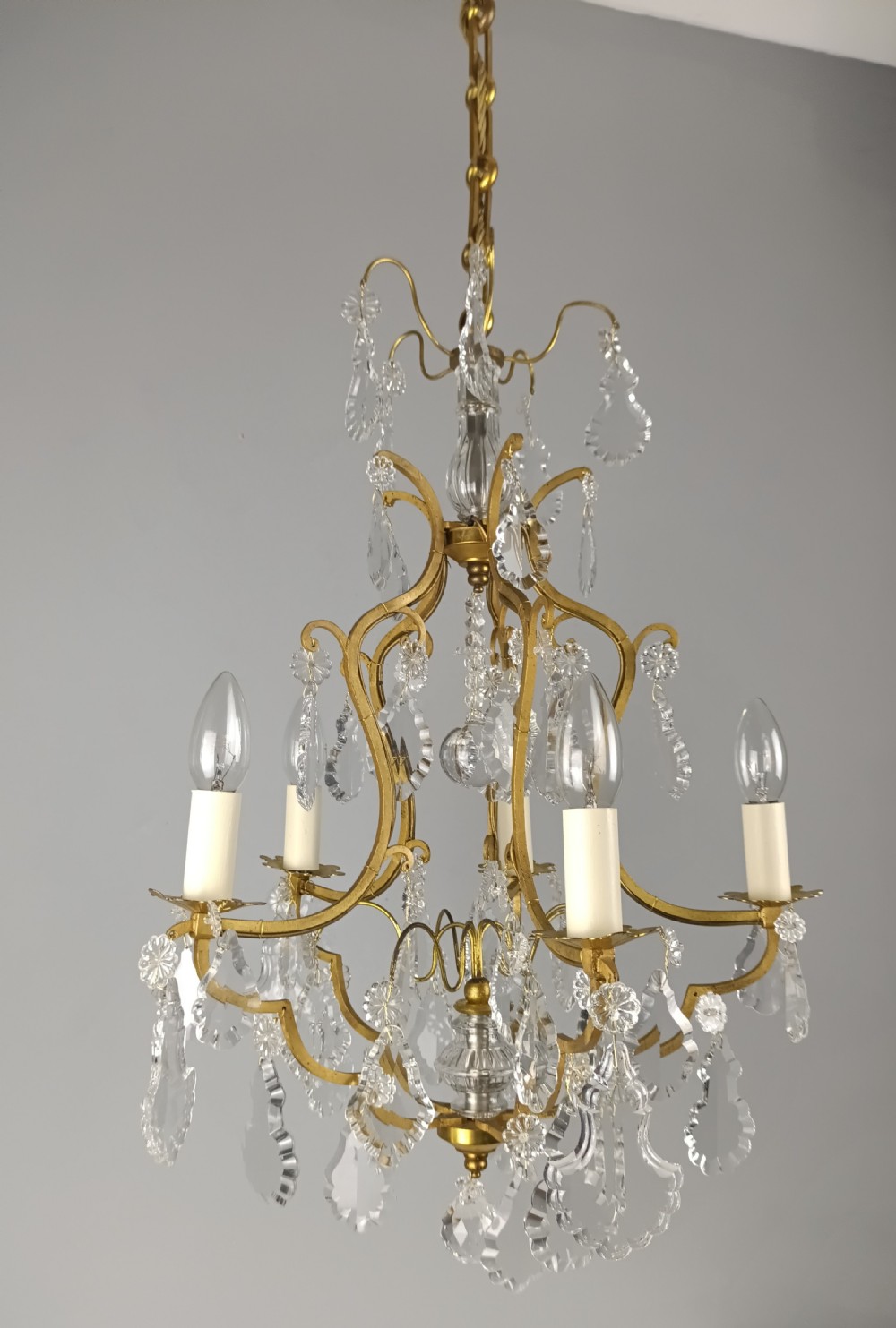 A French Rococo style birdcage chandelier crafted from gilded metal featuring five candle arms adorned with clear cut crystal drops and rosettes. View VIII