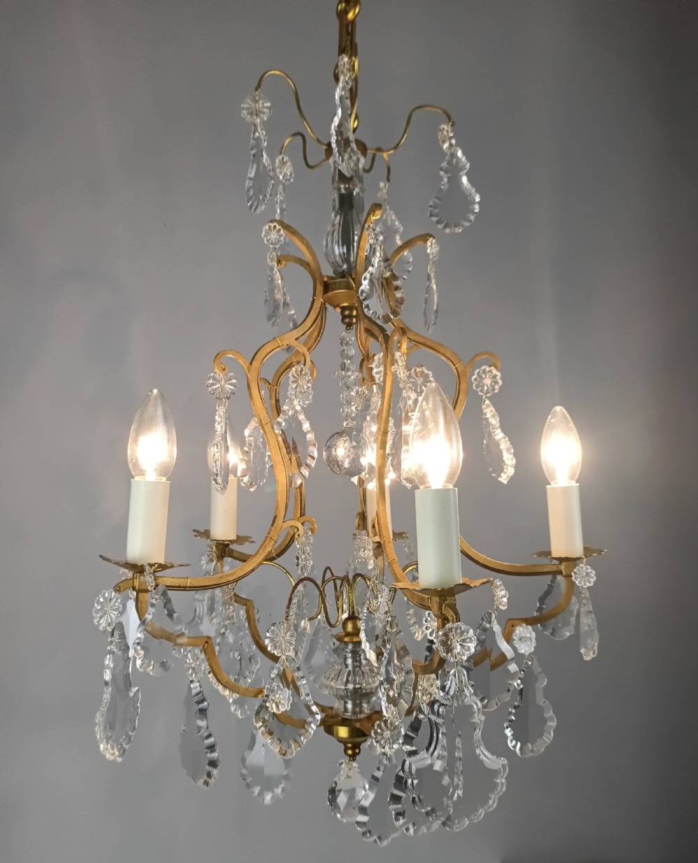 A French Rococo style birdcage chandelier crafted from gilded metal featuring five candle arms adorned with clear cut crystal drops and rosettes. View X