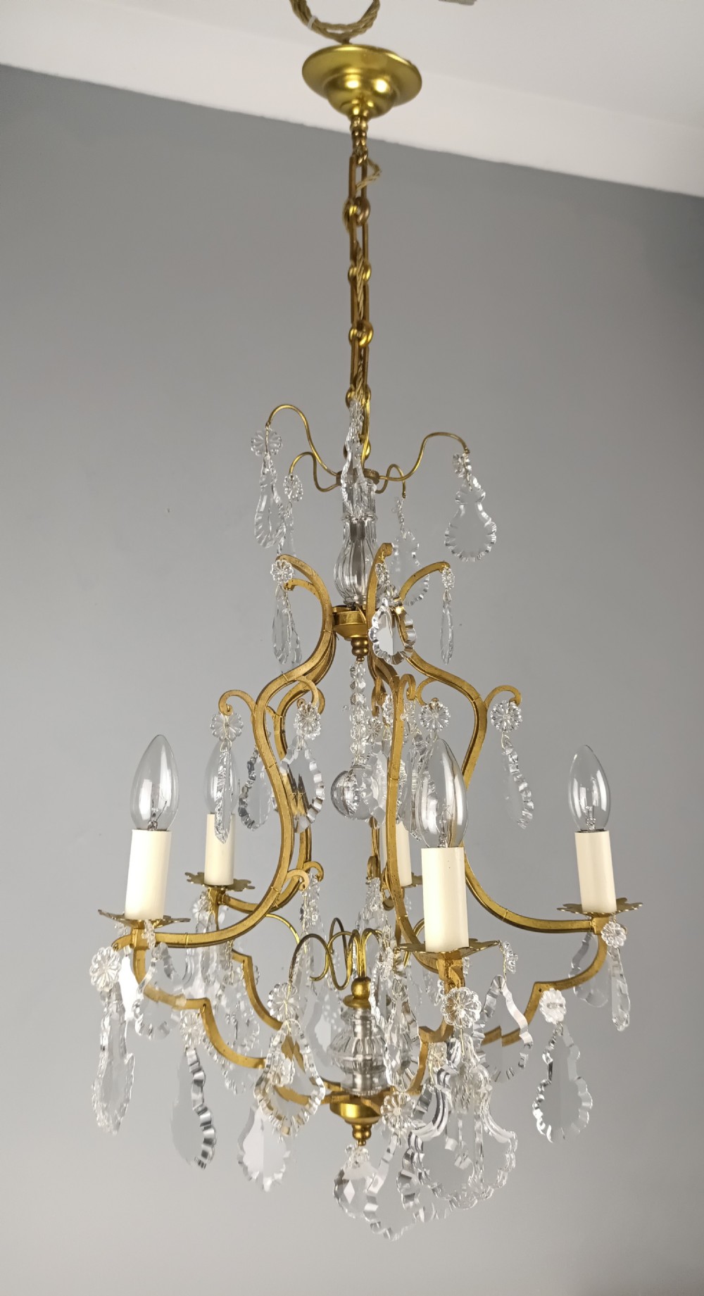 A French Rococo style birdcage chandelier crafted from gilded metal featuring five candle arms adorned with clear cut crystal drops and rosettes. View XI