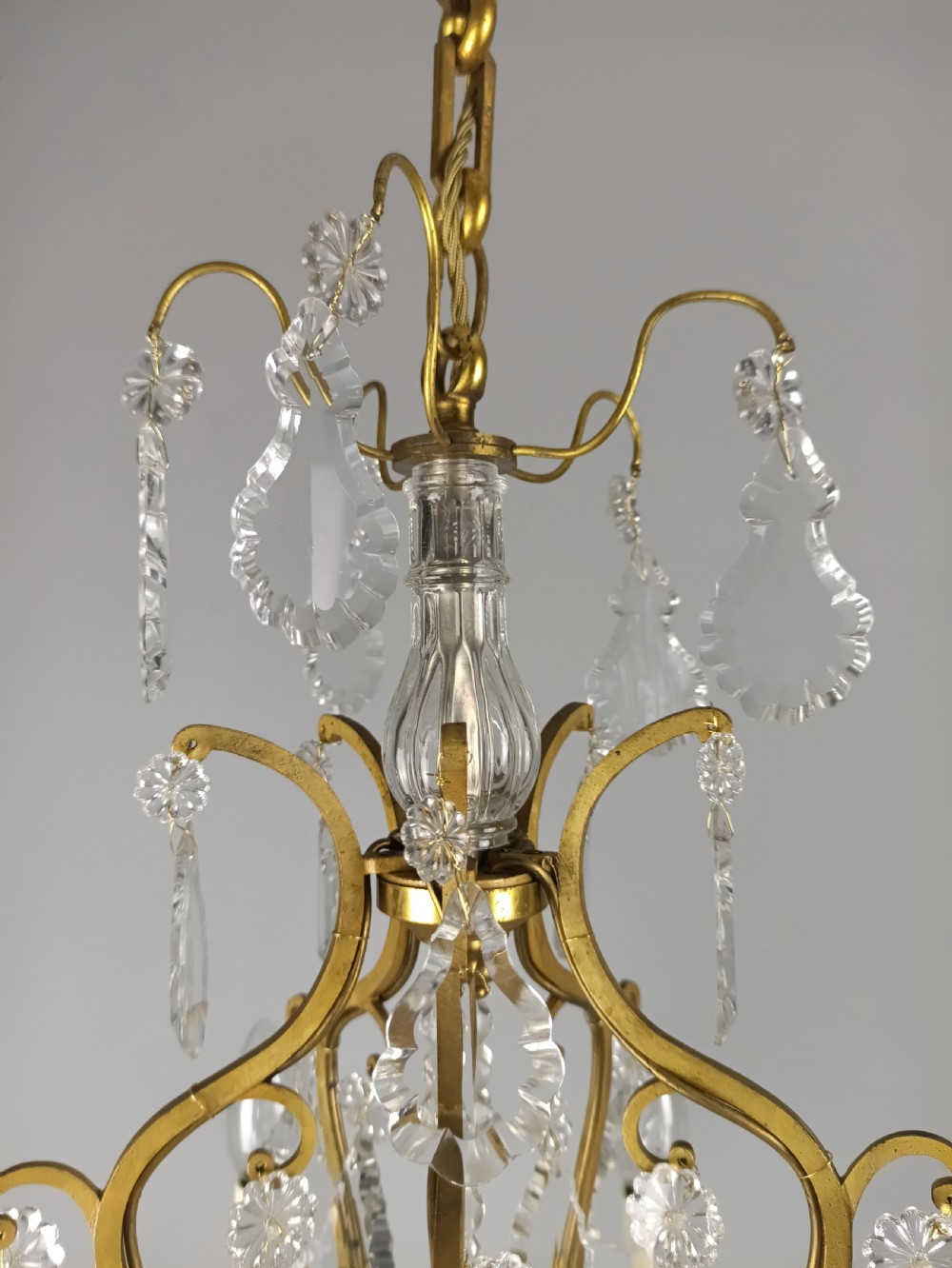 A French Rococo style birdcage chandelier crafted from gilded metal featuring five candle arms adorned with clear cut crystal drops and rosettes. View XII