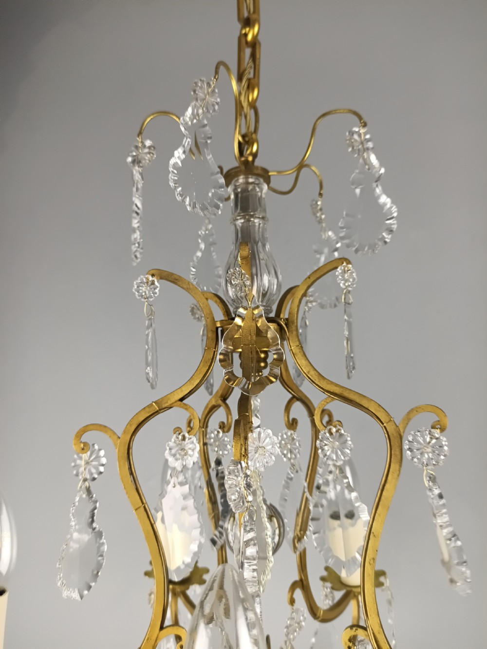 A French Rococo style birdcage chandelier crafted from gilded metal featuring five candle arms adorned with clear cut crystal drops and rosettes. View XIV