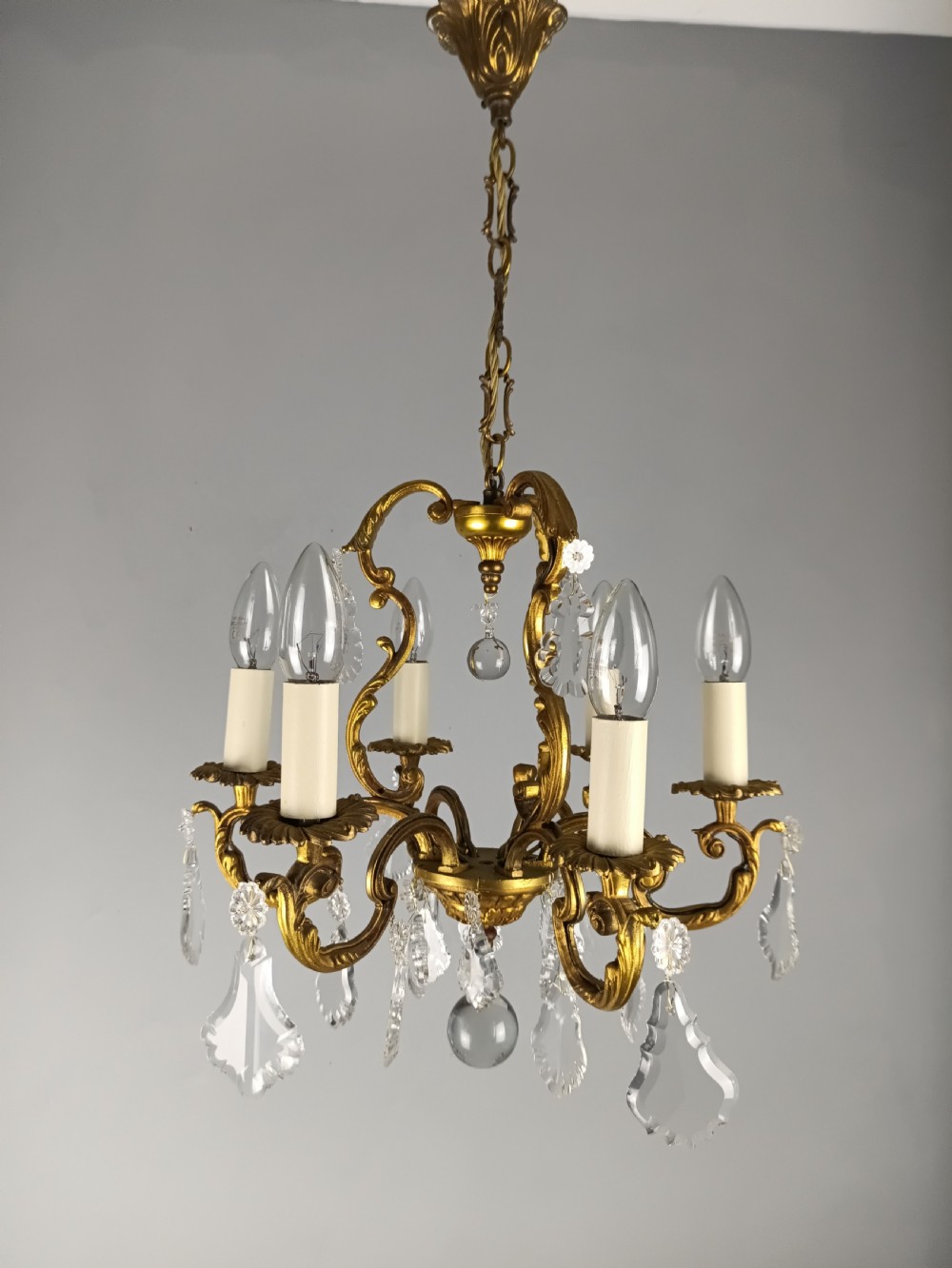 A French six-arm gilded metal chandelier featuring scrolling foliage arms, candle-style bulb holders, and hanging clear cut crystal droplets. View II