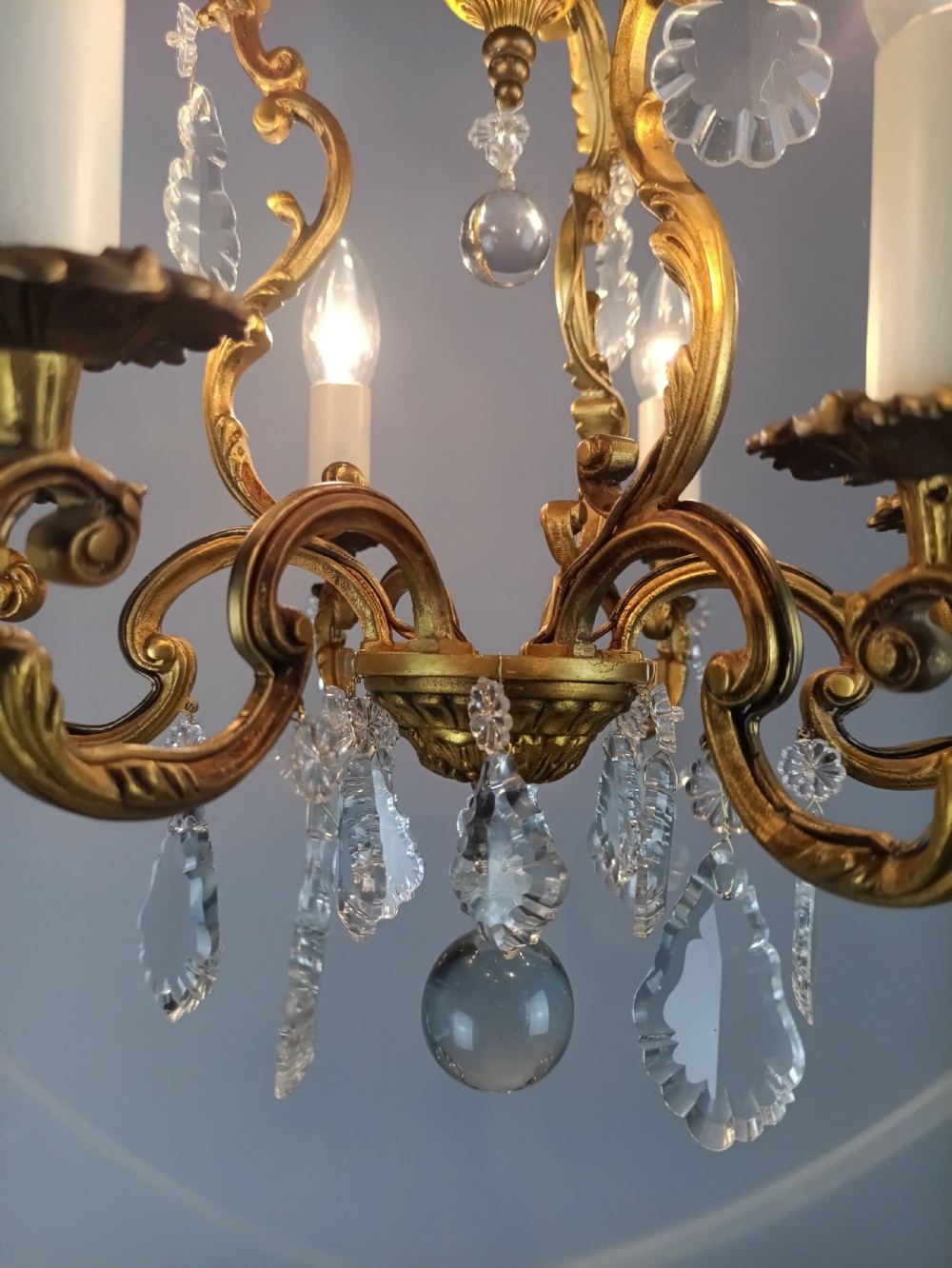 A French six-arm gilded metal chandelier featuring scrolling foliage arms, candle-style bulb holders, and hanging clear cut crystal droplets. View V