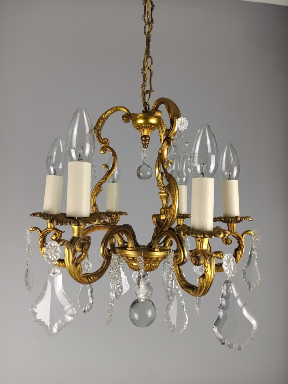 A French six-arm gilded metal chandelier featuring scrolling foliage arms, candle-style bulb holders, and hanging clear cut crystal droplets. View VIII