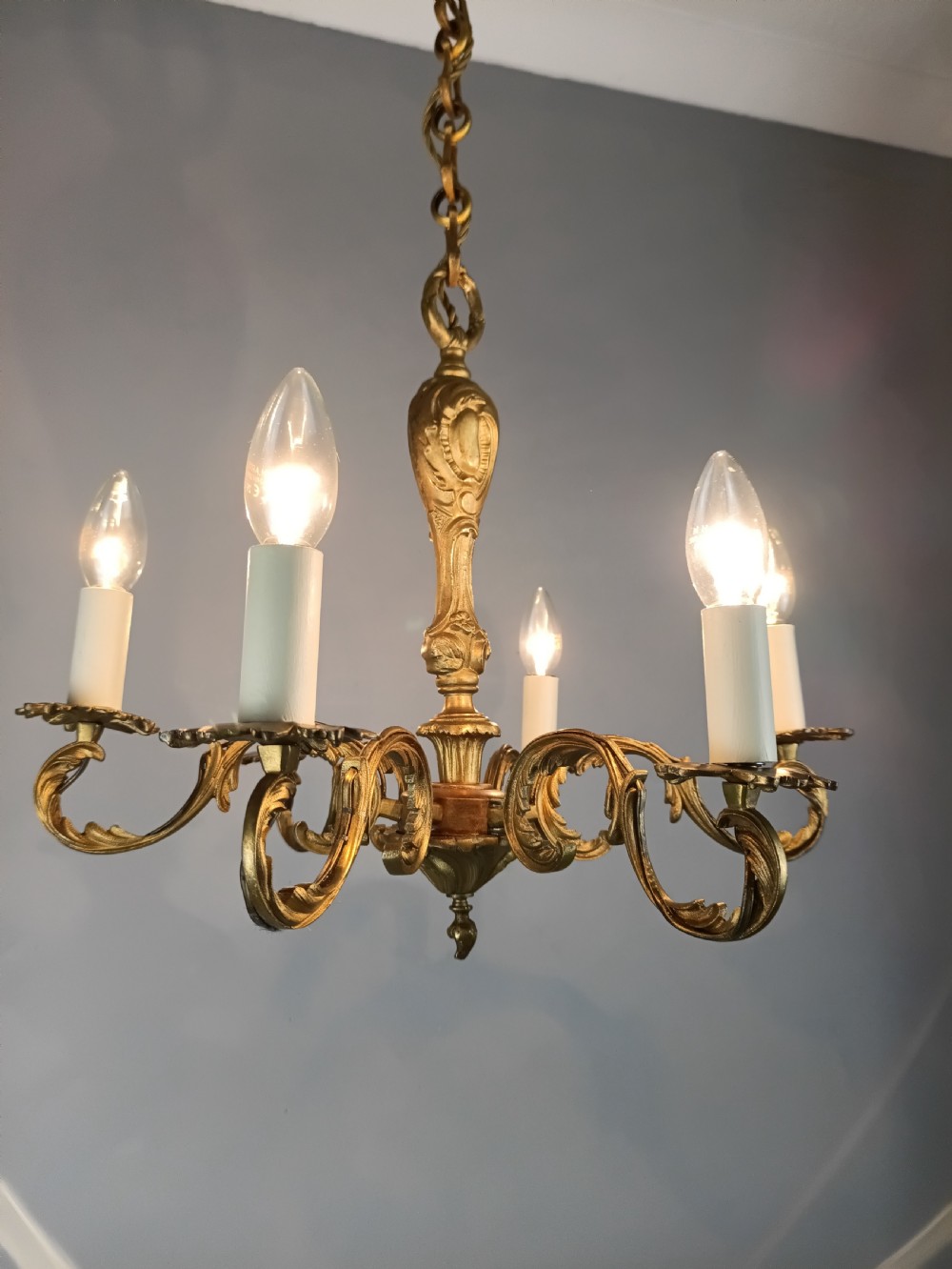 A French gilt brass six-arm chandelier featuring scrolled acanthus leaf branches, cream candle sleeves, and an ornate central column. View IV