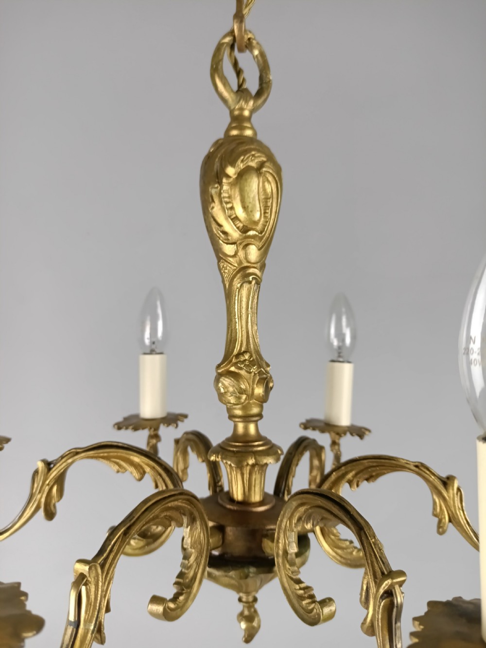 A French gilt brass six-arm chandelier featuring scrolled acanthus leaf branches, cream candle sleeves, and an ornate central column. View VIII