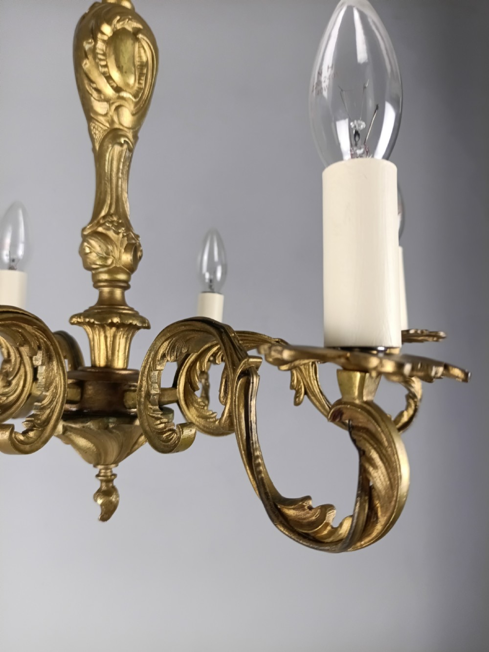 A French gilt brass six-arm chandelier featuring scrolled acanthus leaf branches, cream candle sleeves, and an ornate central column. View IX
