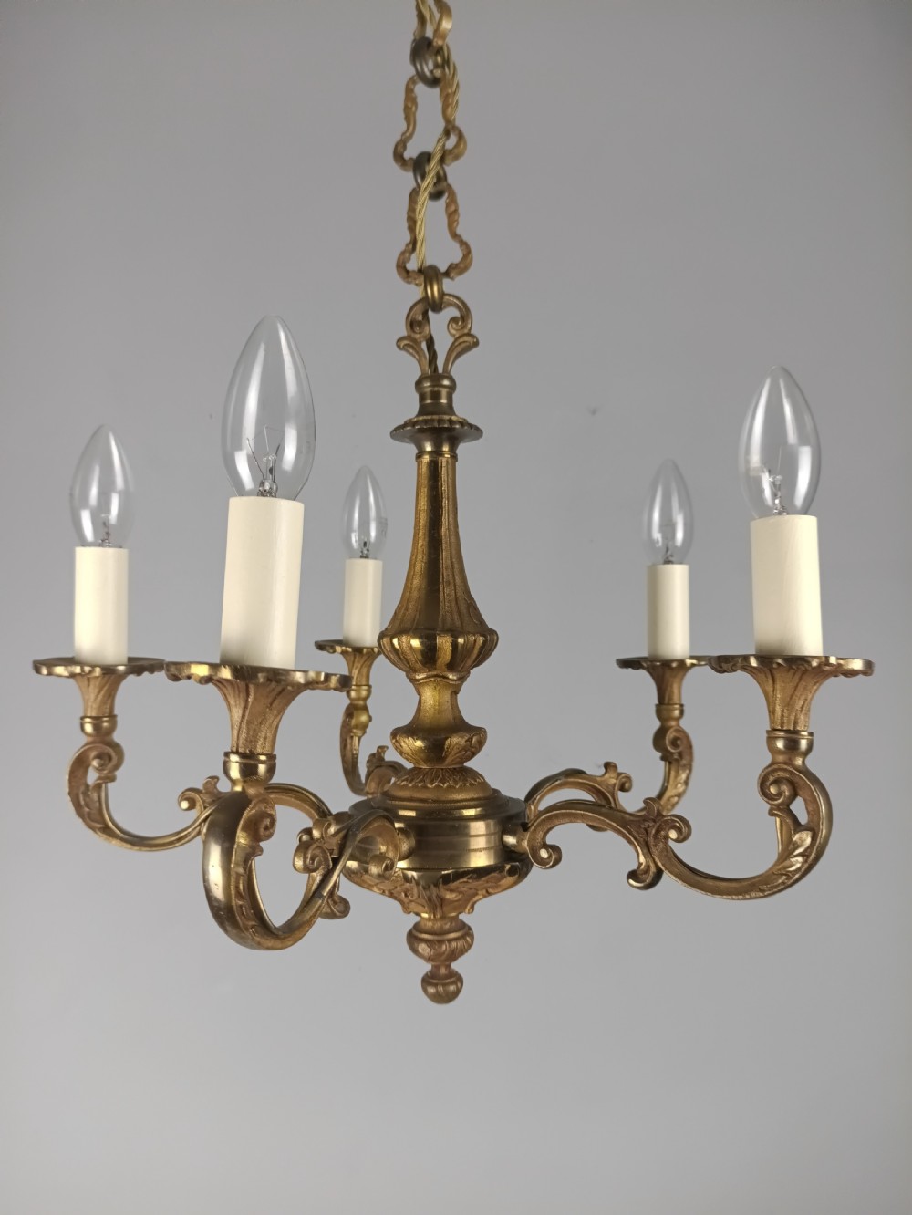 A French gilt brass five-arm chandelier featuring scrolling branch arms, candle bulb sleeves, and an ornate central column.