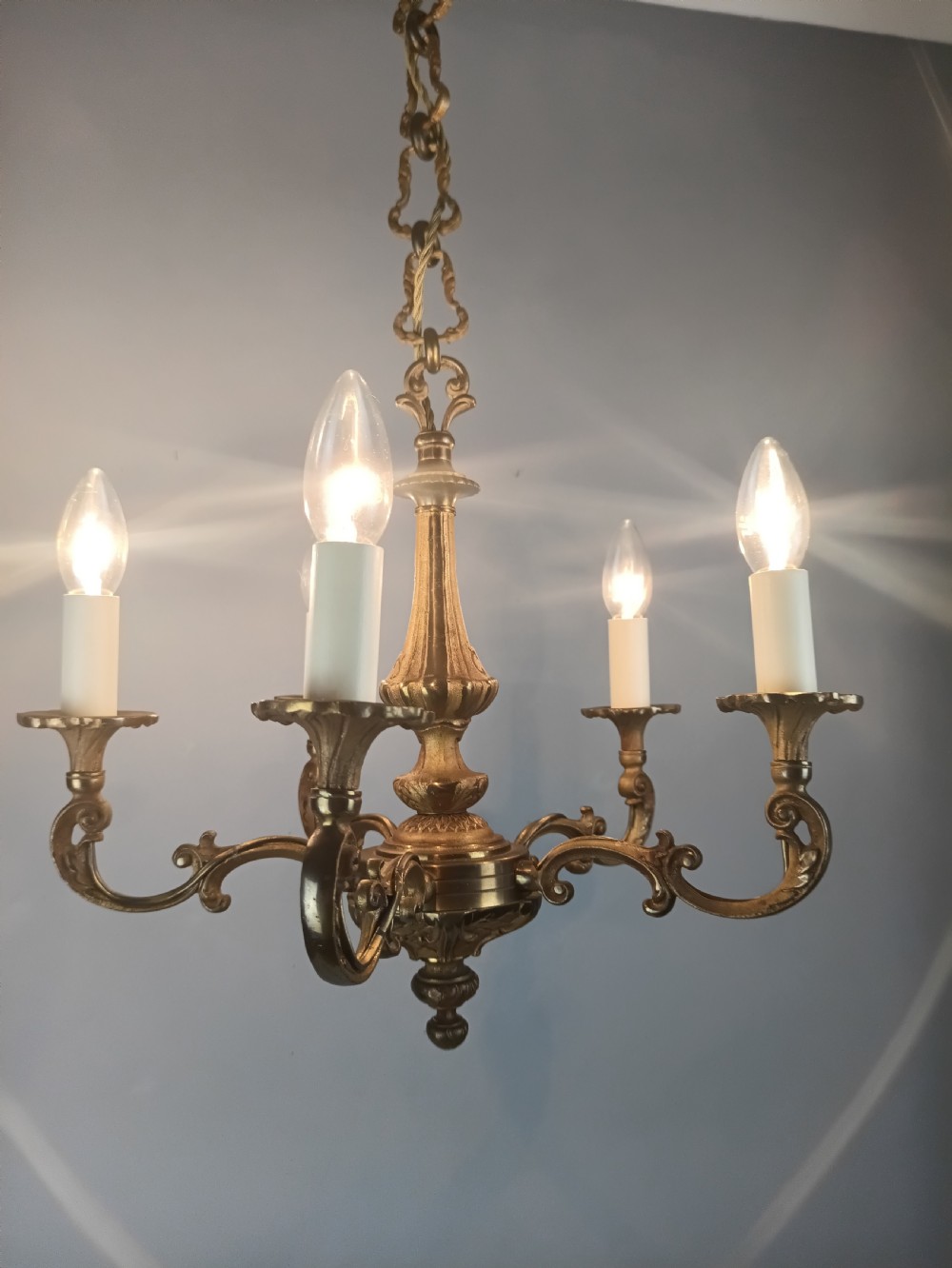 A French gilt brass five-arm chandelier featuring scrolling branch arms, candle bulb sleeves, and an ornate central column. View VI
