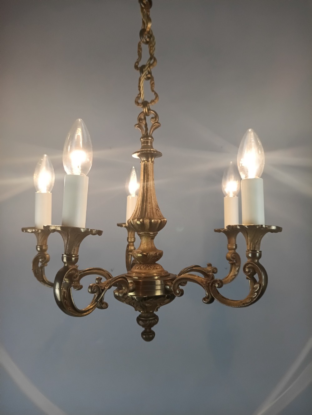 A French gilt brass five-arm chandelier featuring scrolling branch arms, candle bulb sleeves, and an ornate central column. View VII