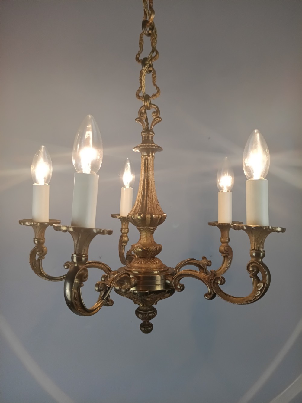 A French gilt brass five-arm chandelier featuring scrolling branch arms, candle bulb sleeves, and an ornate central column. View VIII