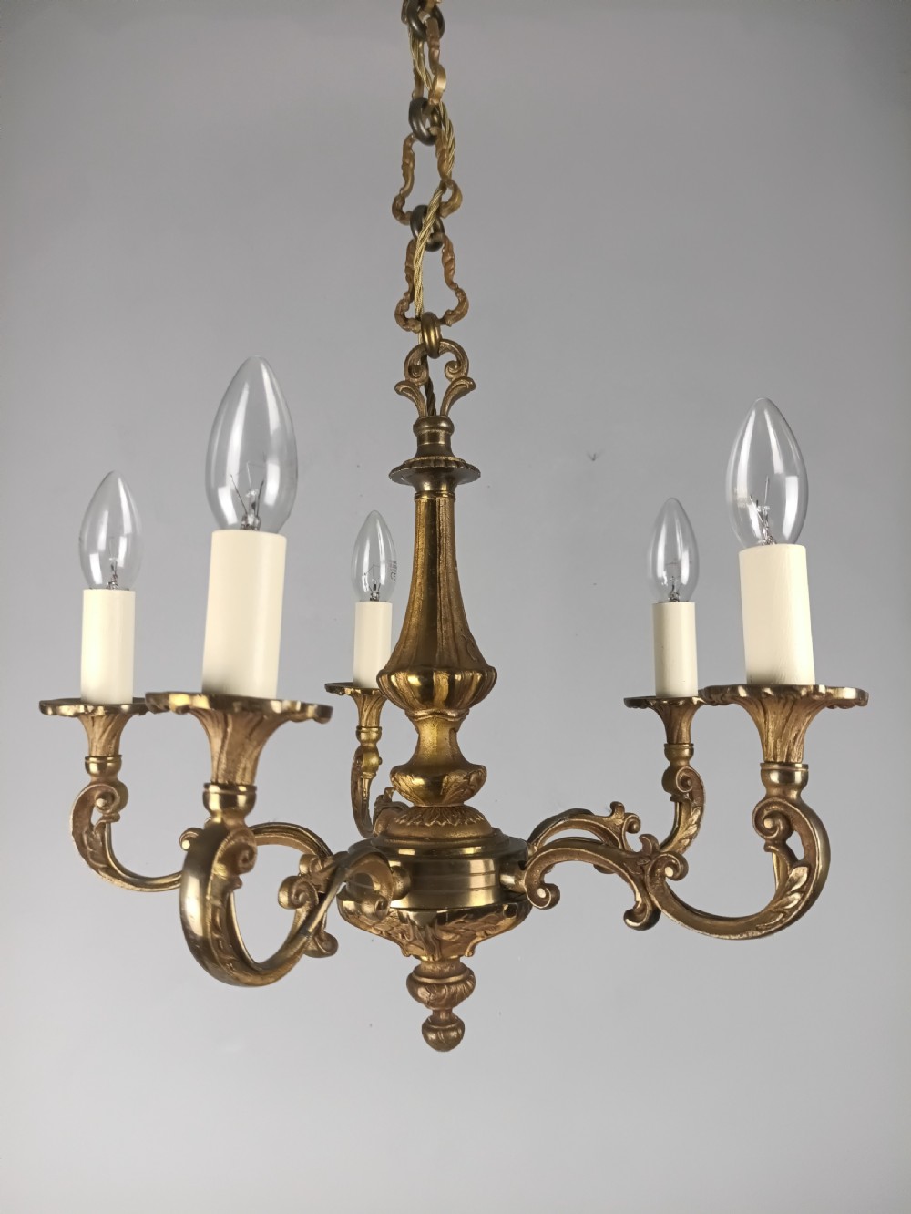 A French gilt brass five-arm chandelier featuring scrolling branch arms, candle bulb sleeves, and an ornate central column. View IX