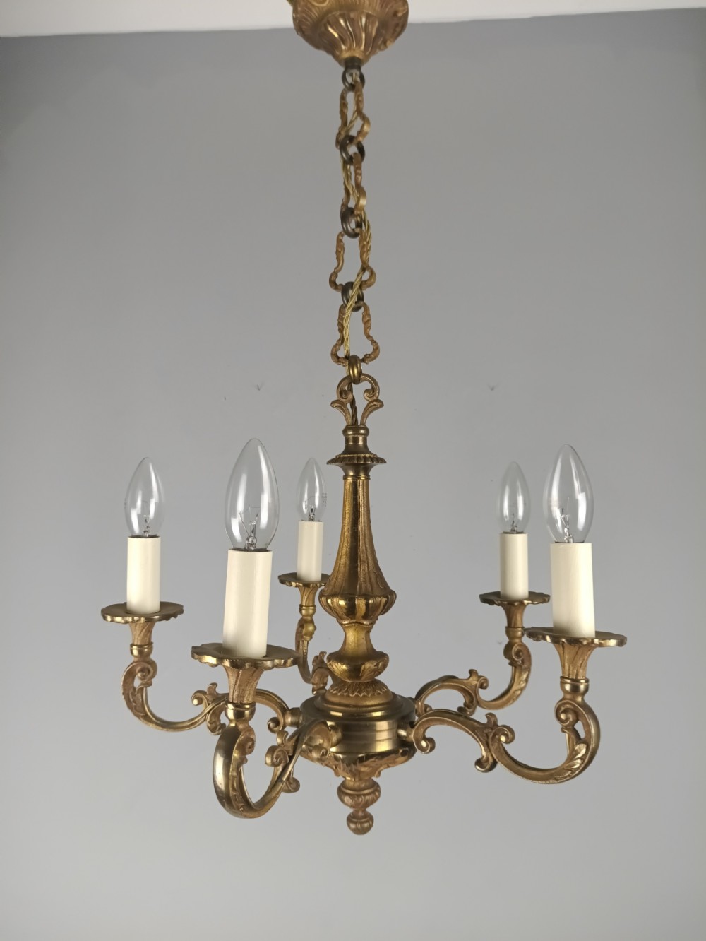 A French gilt brass five-arm chandelier featuring scrolling branch arms, candle bulb sleeves, and an ornate central column. View X