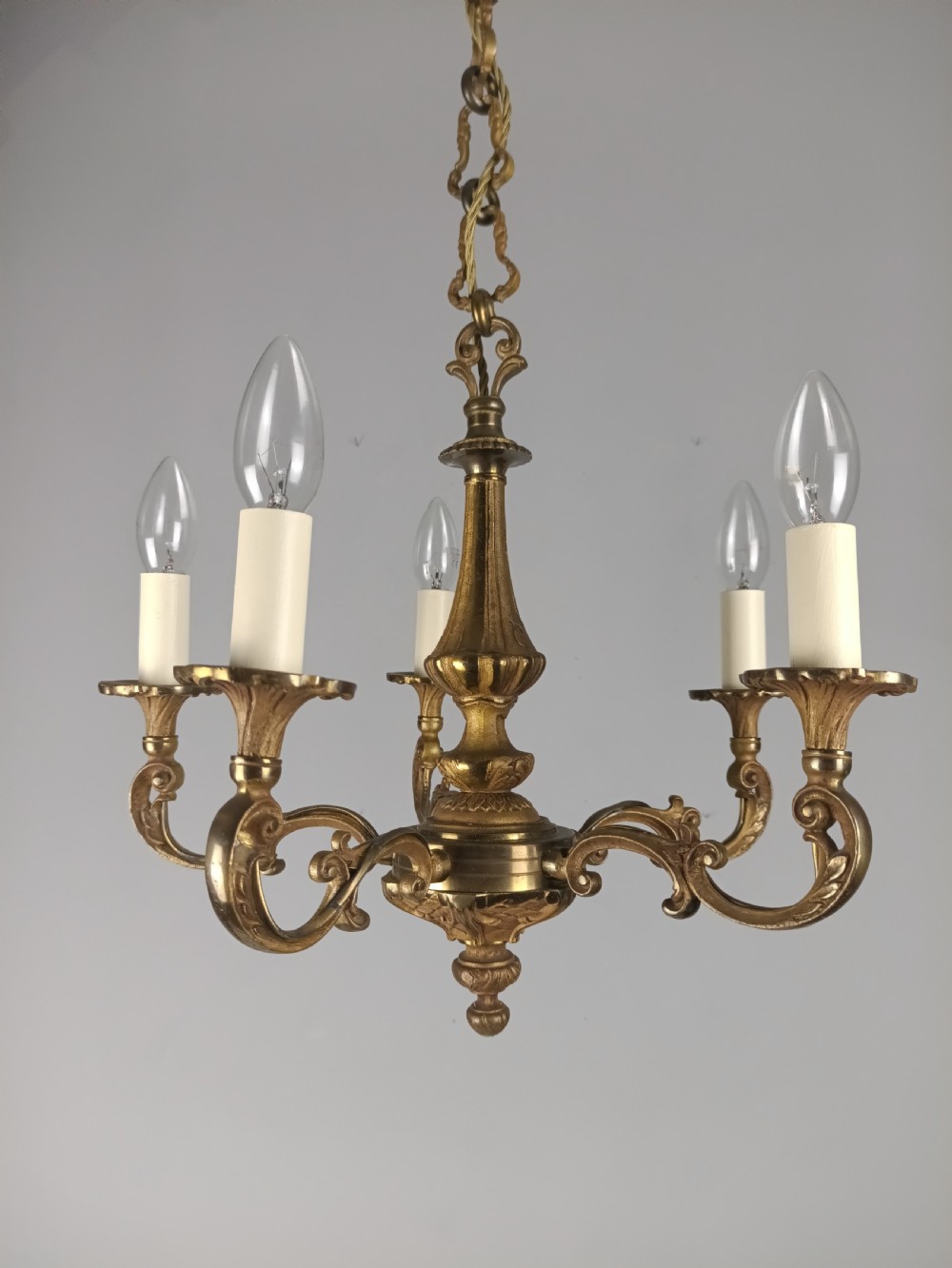 A French gilt brass five-arm chandelier featuring scrolling branch arms, candle bulb sleeves, and an ornate central column. View XV
