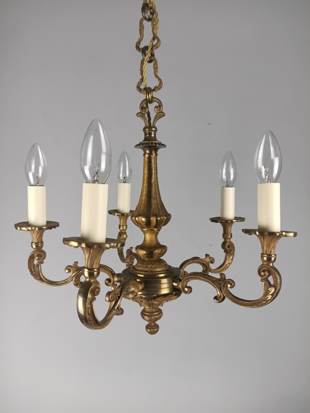 A French gilt brass five-arm chandelier featuring scrolling branch arms, candle bulb sleeves, and an ornate central column. View XVI