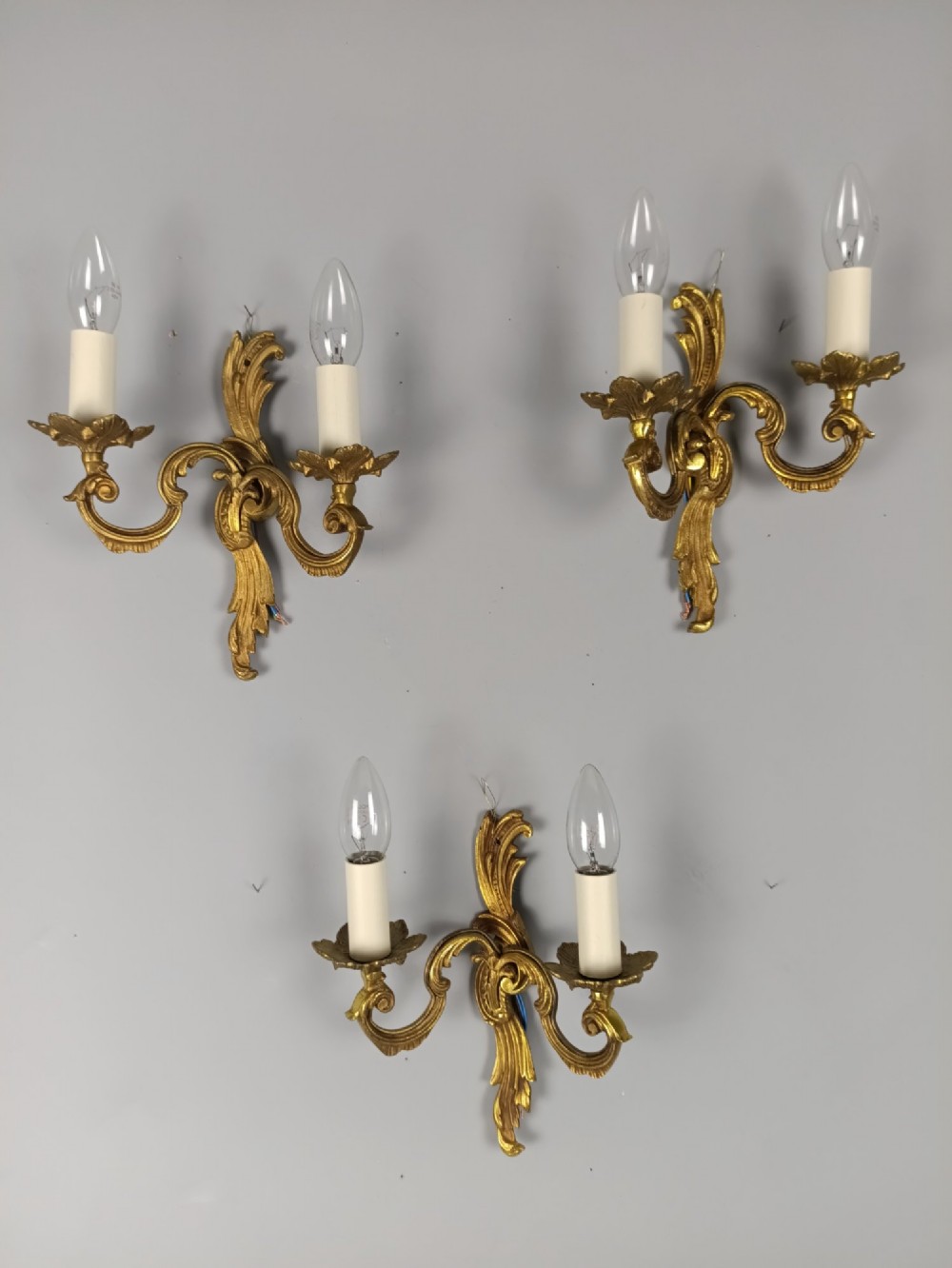 Set of three French gilt metal twin-arm wall sconces featuring acanthus leaf motifs and cream candle-style bulb sleeves. View II