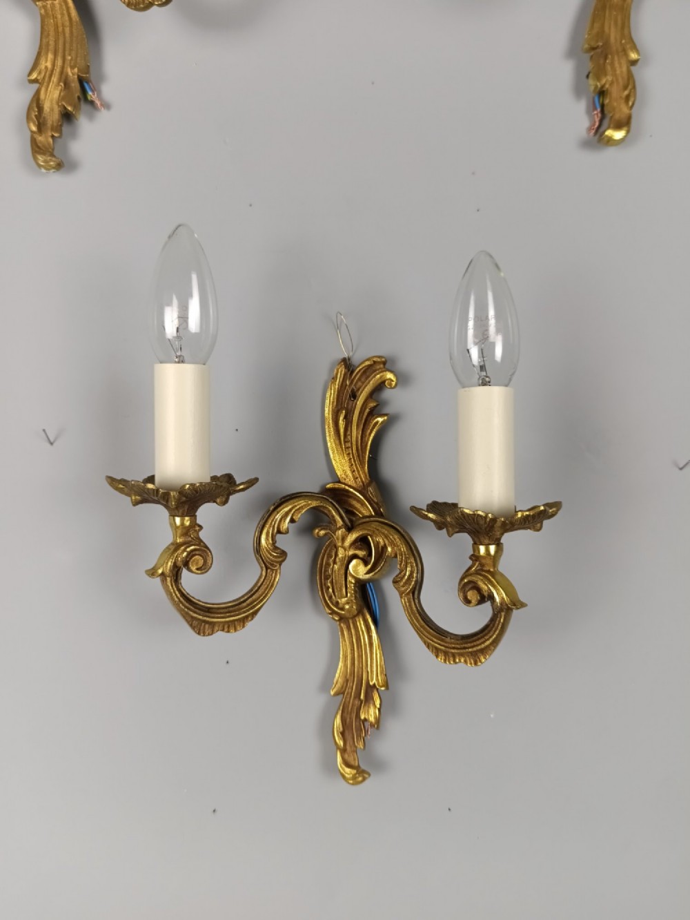 Set of three French gilt metal twin-arm wall sconces featuring acanthus leaf motifs and cream candle-style bulb sleeves. View III