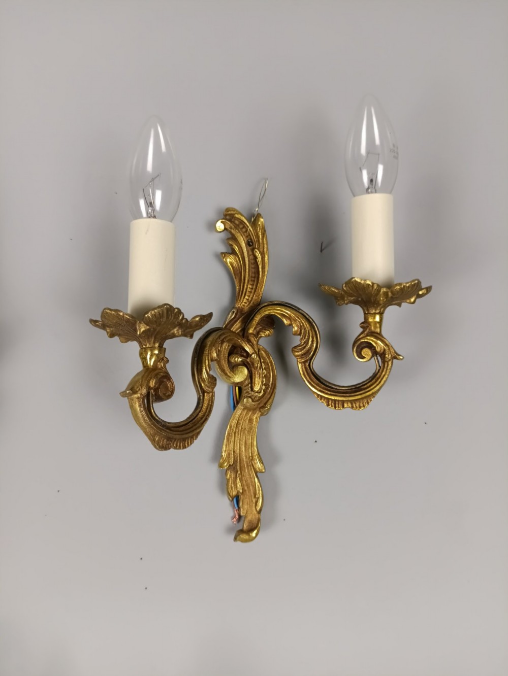 Set of three French gilt metal twin-arm wall sconces featuring acanthus leaf motifs and cream candle-style bulb sleeves. View IV