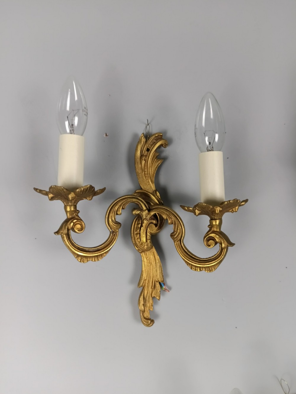 Set of three French gilt metal twin-arm wall sconces featuring acanthus leaf motifs and cream candle-style bulb sleeves. View V