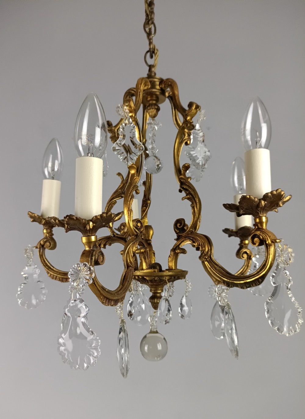 A French five-light gilded brass frame chandelier featuring scrolled arms, candle sleeves, and suspended cut crystal drops.