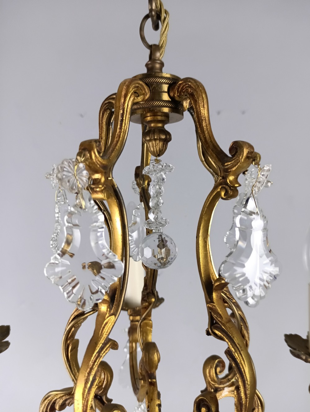 A French five-light gilded brass frame chandelier featuring scrolled arms, candle sleeves, and suspended cut crystal drops. View II