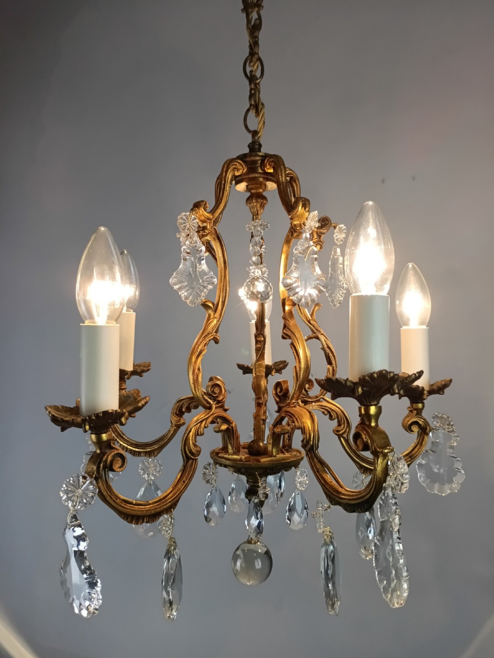 A French five-light gilded brass frame chandelier featuring scrolled arms, candle sleeves, and suspended cut crystal drops. View III