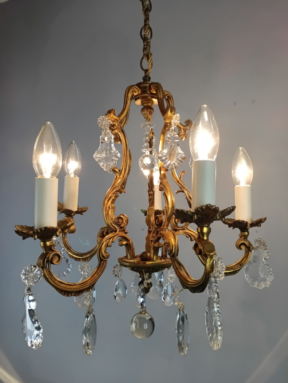 A French five-light gilded brass frame chandelier featuring scrolled arms, candle sleeves, and suspended cut crystal drops. View IV