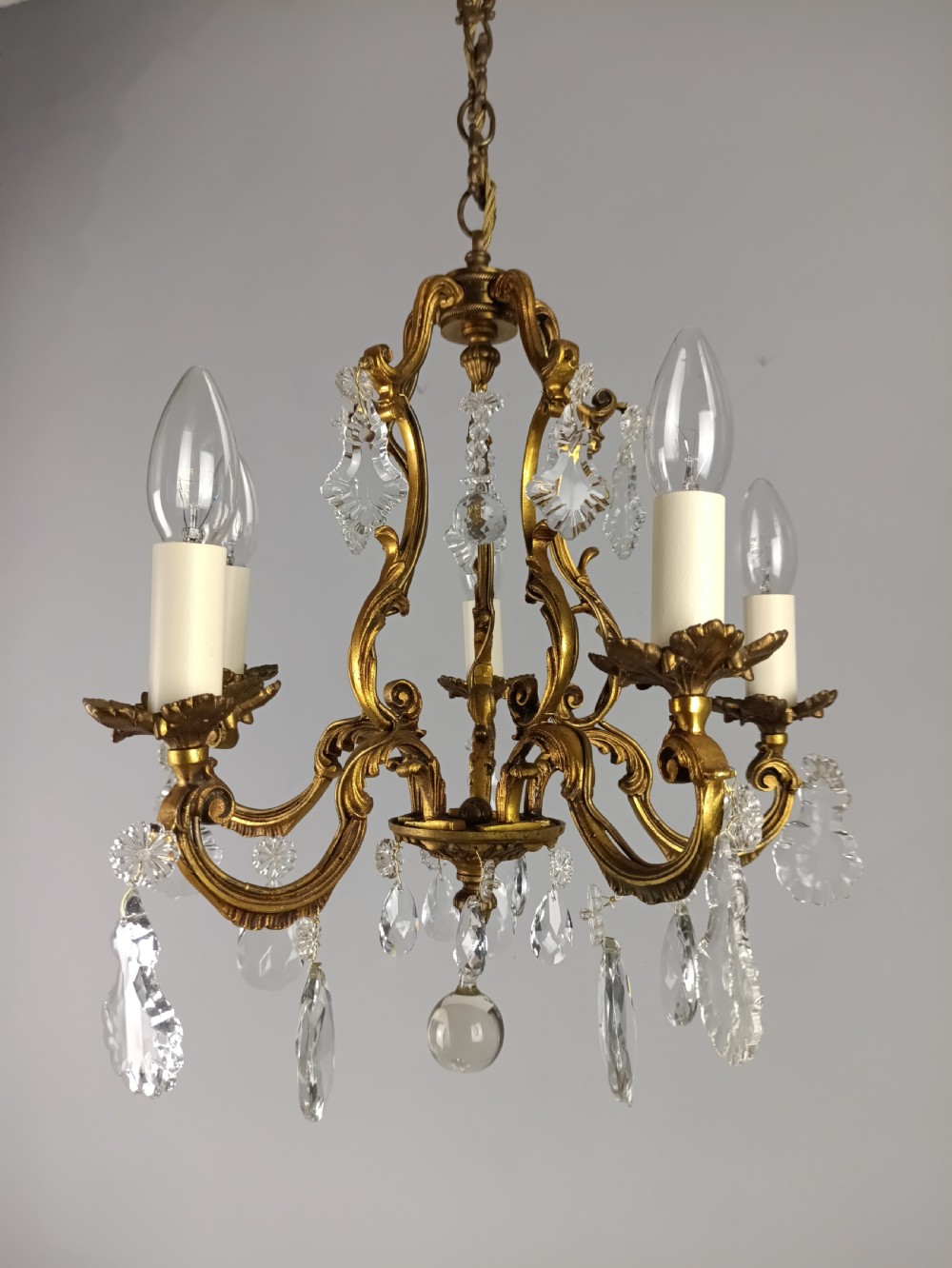 A French five-light gilded brass frame chandelier featuring scrolled arms, candle sleeves, and suspended cut crystal drops. View VI
