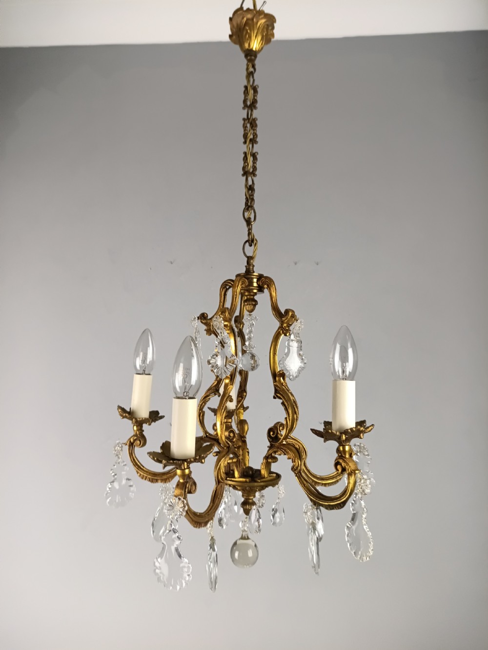 A French five-light gilded brass frame chandelier featuring scrolled arms, candle sleeves, and suspended cut crystal drops. View VII