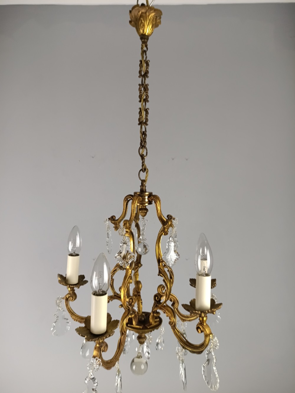 A French five-light gilded brass frame chandelier featuring scrolled arms, candle sleeves, and suspended cut crystal drops. View VIII