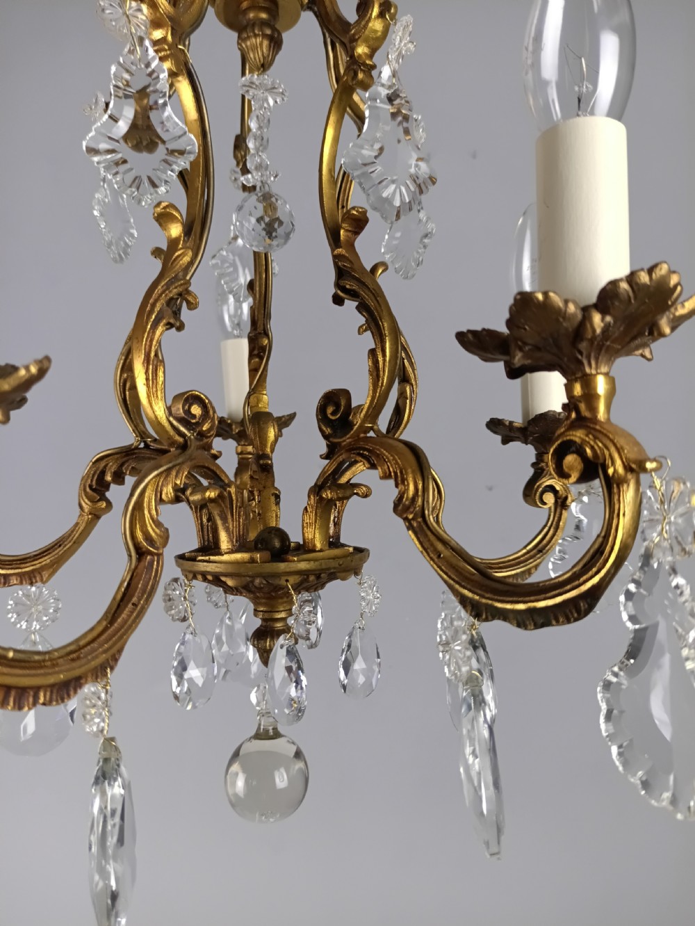 A French five-light gilded brass frame chandelier featuring scrolled arms, candle sleeves, and suspended cut crystal drops. View X
