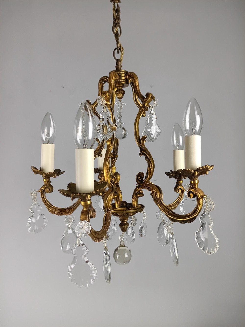 A French five-light gilded brass frame chandelier featuring scrolled arms, candle sleeves, and suspended cut crystal drops. View XI