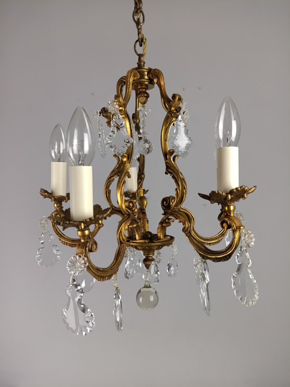 A French five-light gilded brass frame chandelier featuring scrolled arms, candle sleeves, and suspended cut crystal drops. View XII