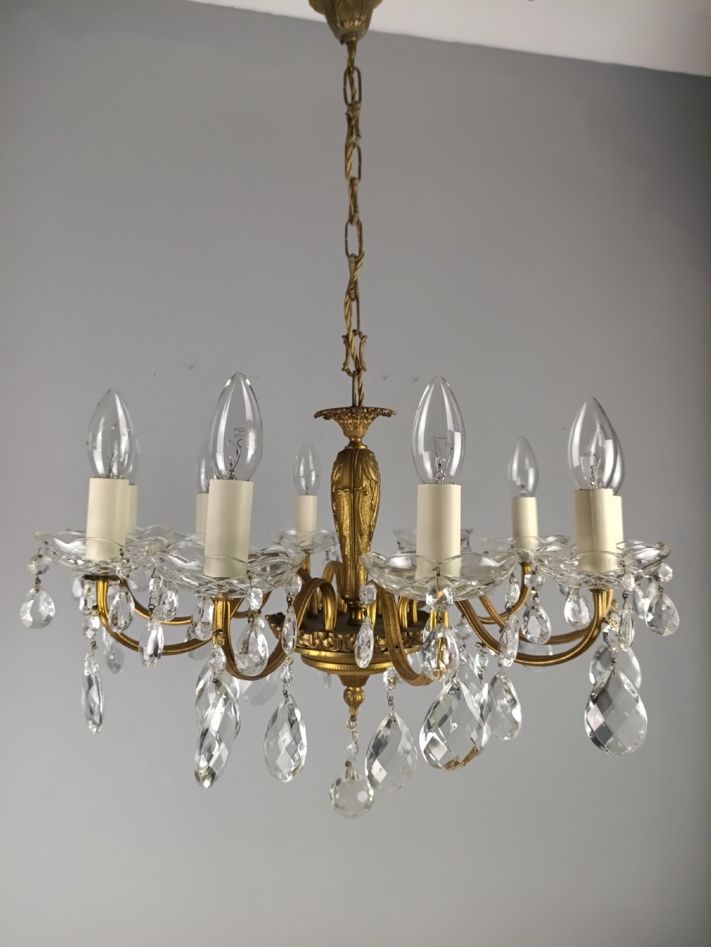 A French style gilt brass ten-light chandelier featuring curved candle arms, glass bobeches, and faceted hanging glass drops.