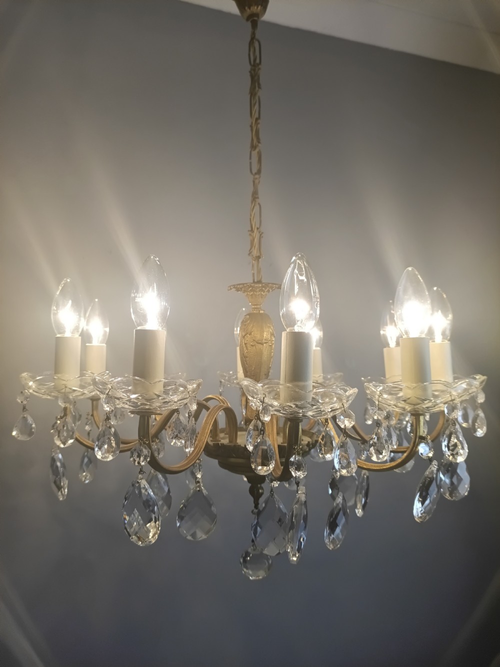 A French style gilt brass ten-light chandelier featuring curved candle arms, glass bobeches, and faceted hanging glass drops. View VI