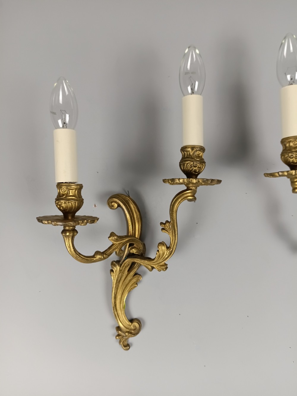 A pair of French gilt brass two-arm wall sconces featuring ornate acanthus leaf scrollwork and faux candle sleeve fittings. View II