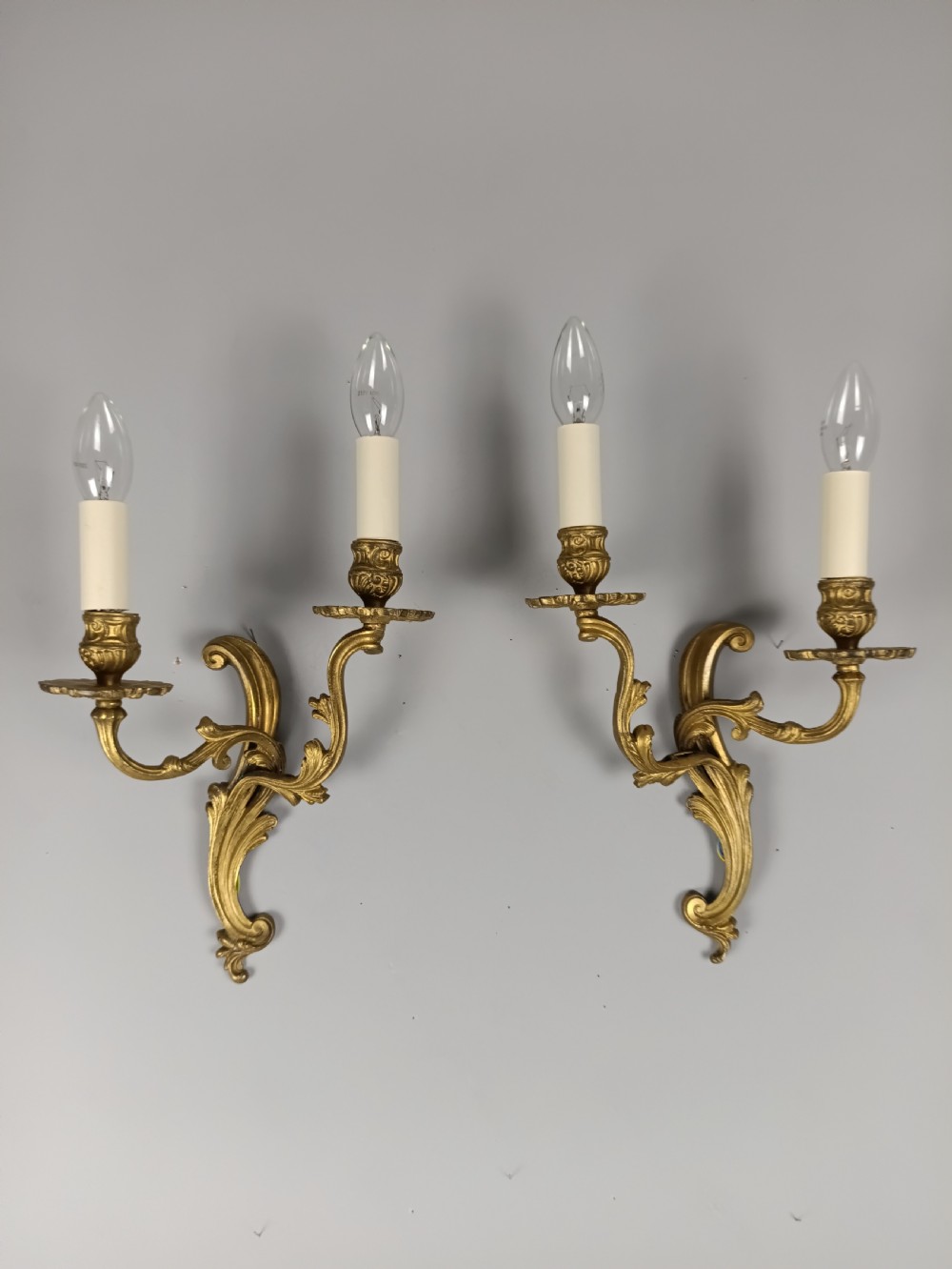 A pair of French gilt brass two-arm wall sconces featuring ornate acanthus leaf scrollwork and faux candle sleeve fittings. View IV