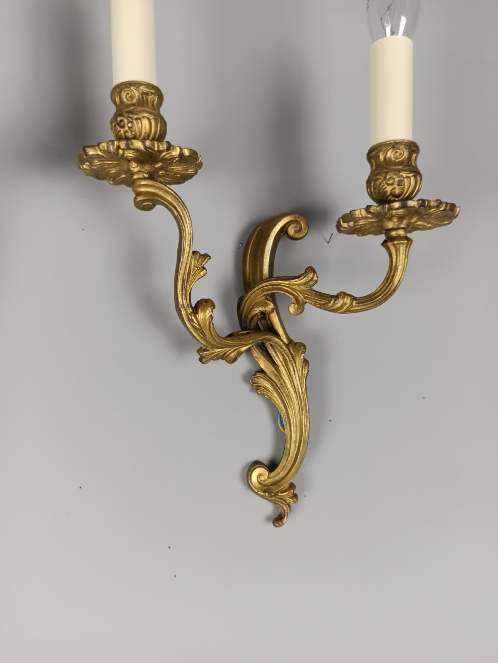 A pair of French gilt brass two-arm wall sconces featuring ornate acanthus leaf scrollwork and faux candle sleeve fittings. View V