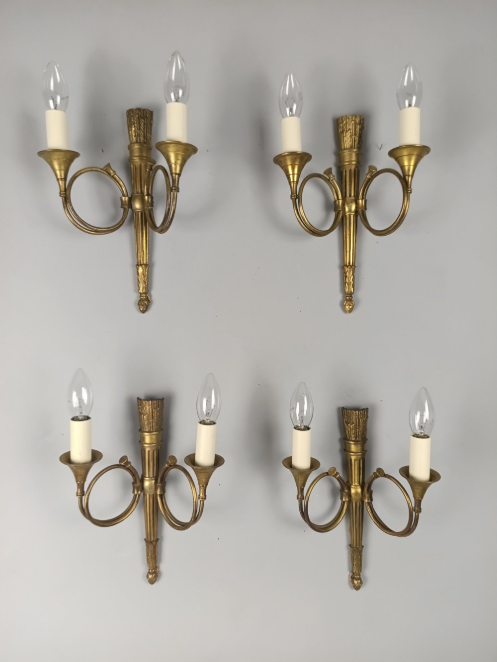 A set of four French Empire style gilt brass wall lights, each featuring two curved hunting horn arms extending from a central torch-form backplate.