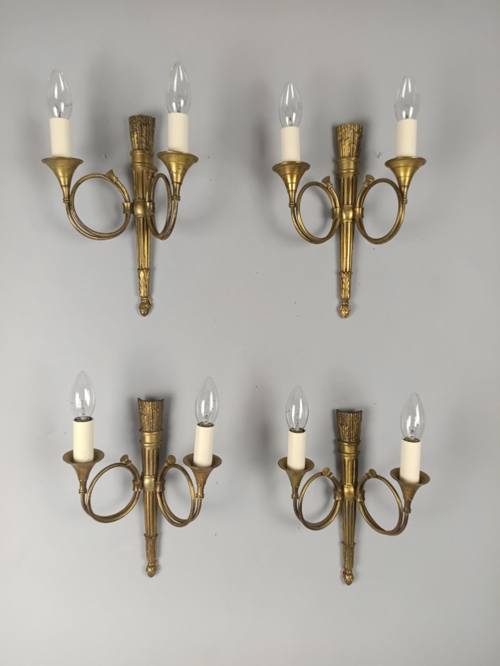 A set of four French Empire style gilt brass wall lights, each featuring two curved hunting horn arms extending from a central torch-form backplate. View V