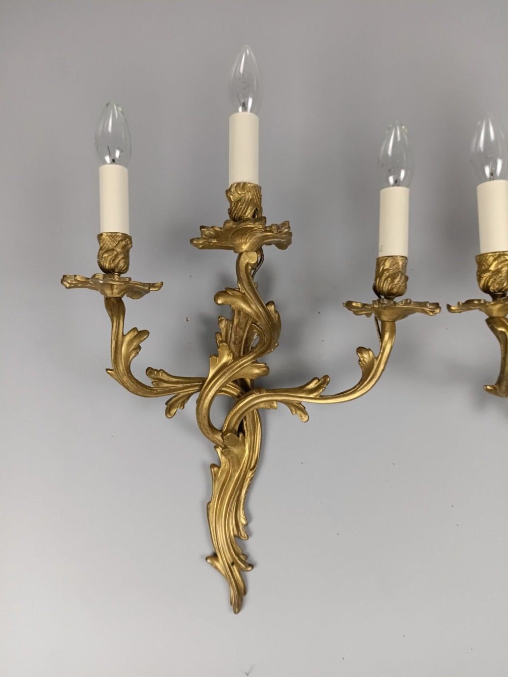 A pair of antique French Rococo gilded bronze triple-arm wall sconces featuring acanthus leaf scrollwork and candle sleeves. View II