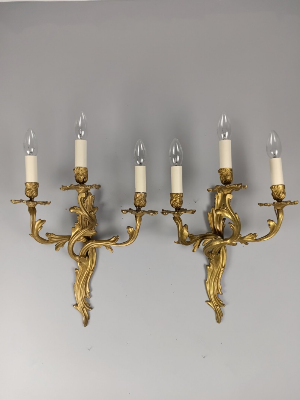 A pair of antique French Rococo gilded bronze triple-arm wall sconces featuring acanthus leaf scrollwork and candle sleeves. View III