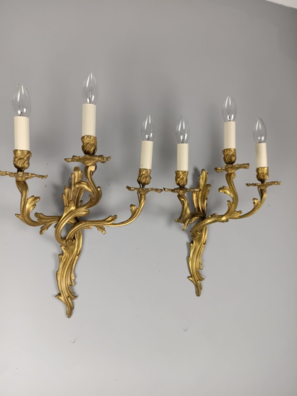 A pair of antique French Rococo gilded bronze triple-arm wall sconces featuring acanthus leaf scrollwork and candle sleeves. View IV
